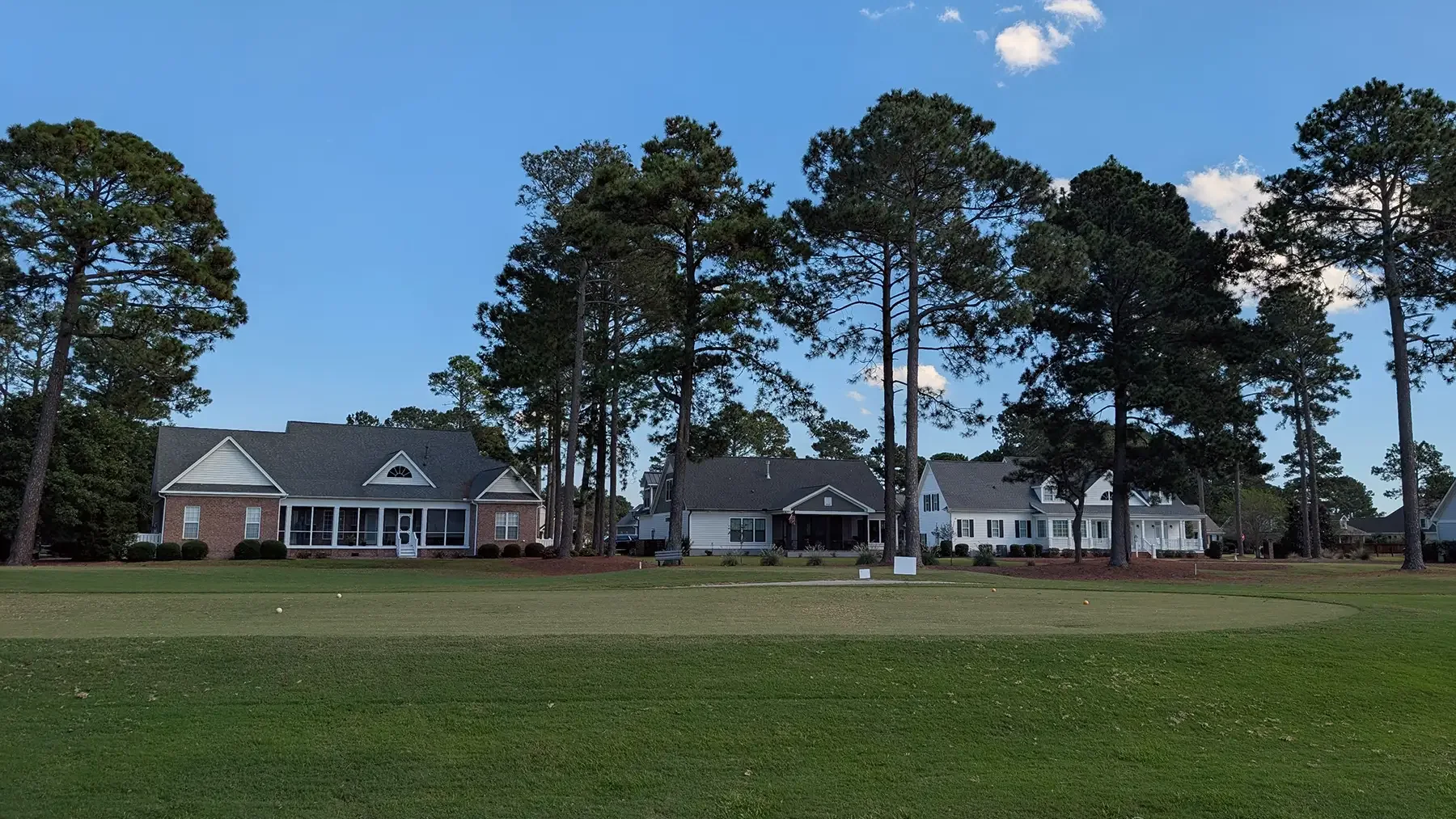 Brick and sided homes behind a golf green under tall pines in Magnolia Greens, Leland, NC