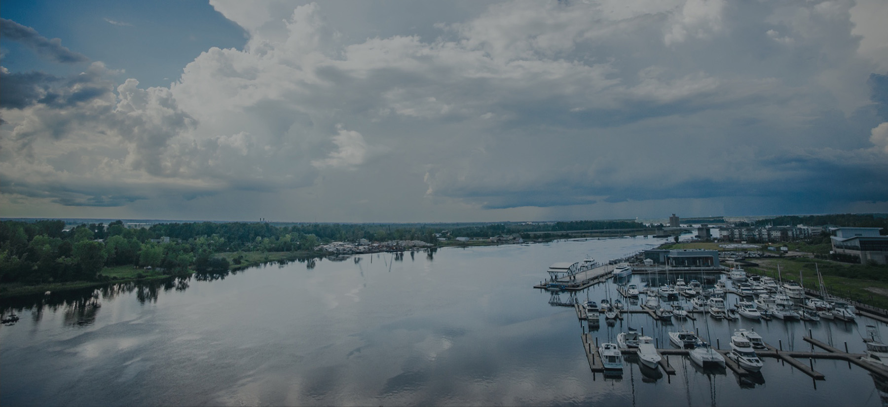 Boats moored along a broad river beneath a cloud-filled sky