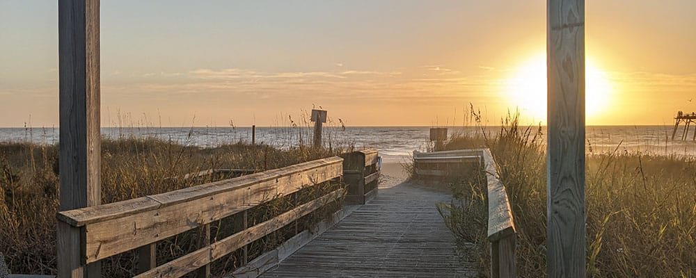 Wooden beach walkway framed by dunes and the rising sun