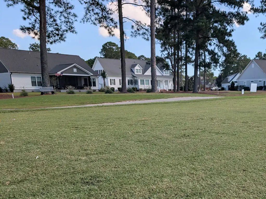 Fairway in front of white and gray homes under tall pines in Magnolia Greens, Leland, NC