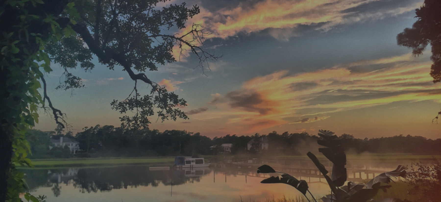 A quiet waterfront and dock framed by trees at sunset