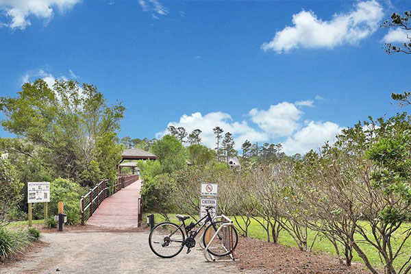 Wooden boardwalk leading to a gazebo along a park trail, with a bicycle at a rack in the foreground